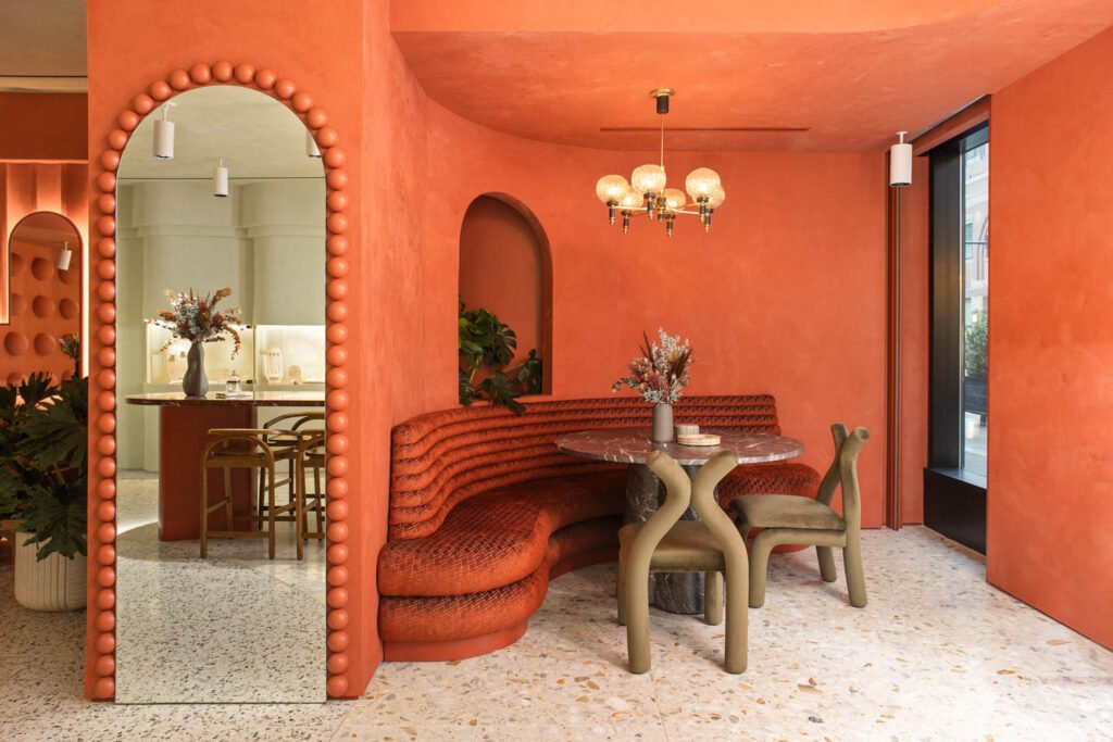 a red booth curves around a deep red wall near a full length mirror and a round table