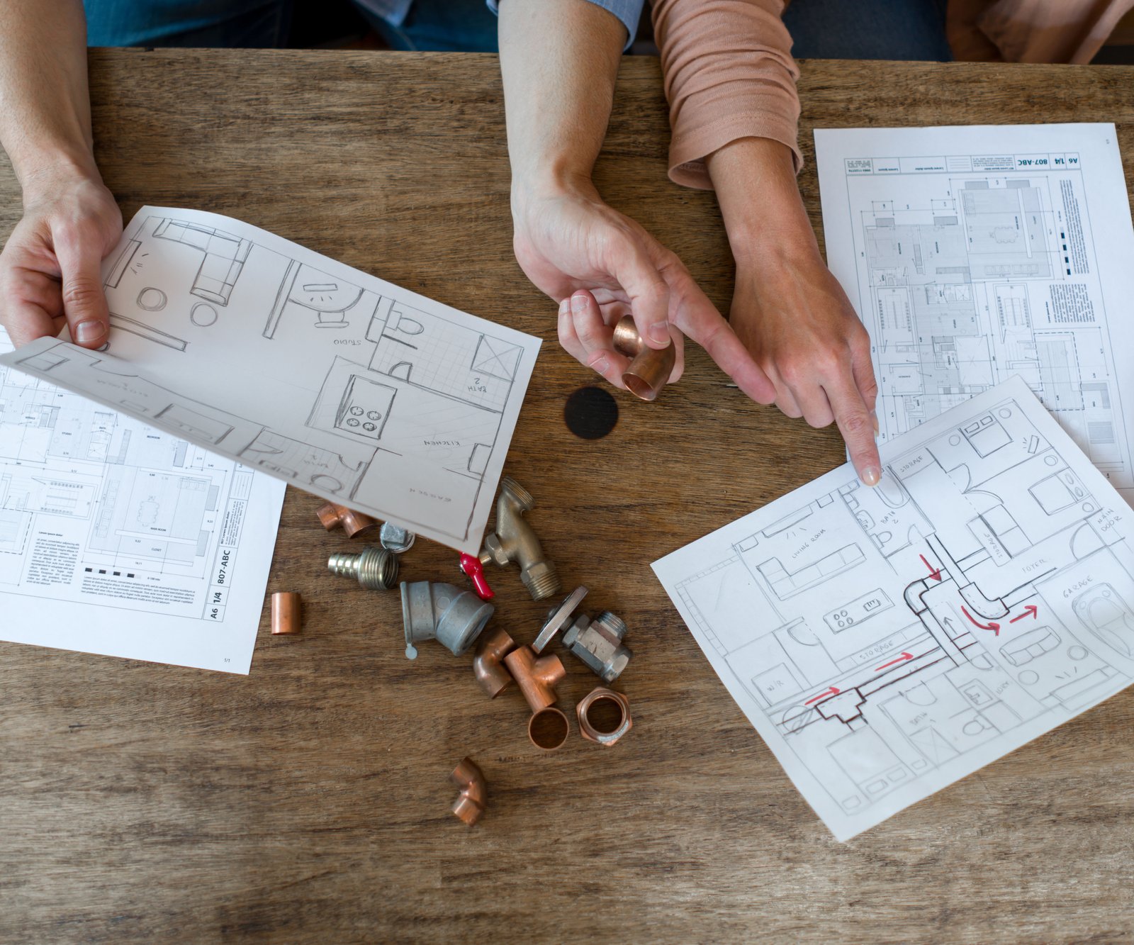 hands holding pieces of pipe fitting over architectural type drawings