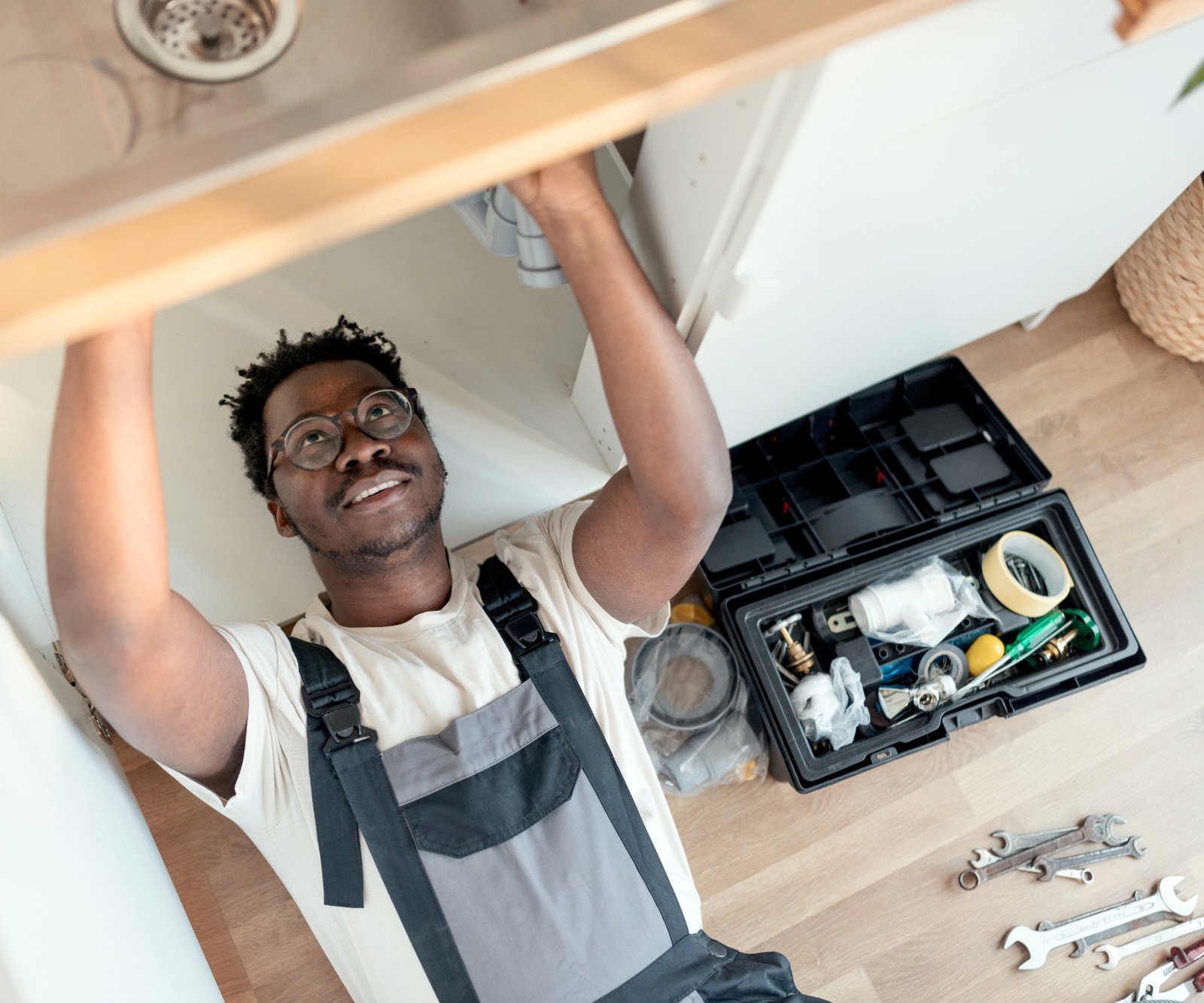 plumber lying with head in cupboard fitting a sink