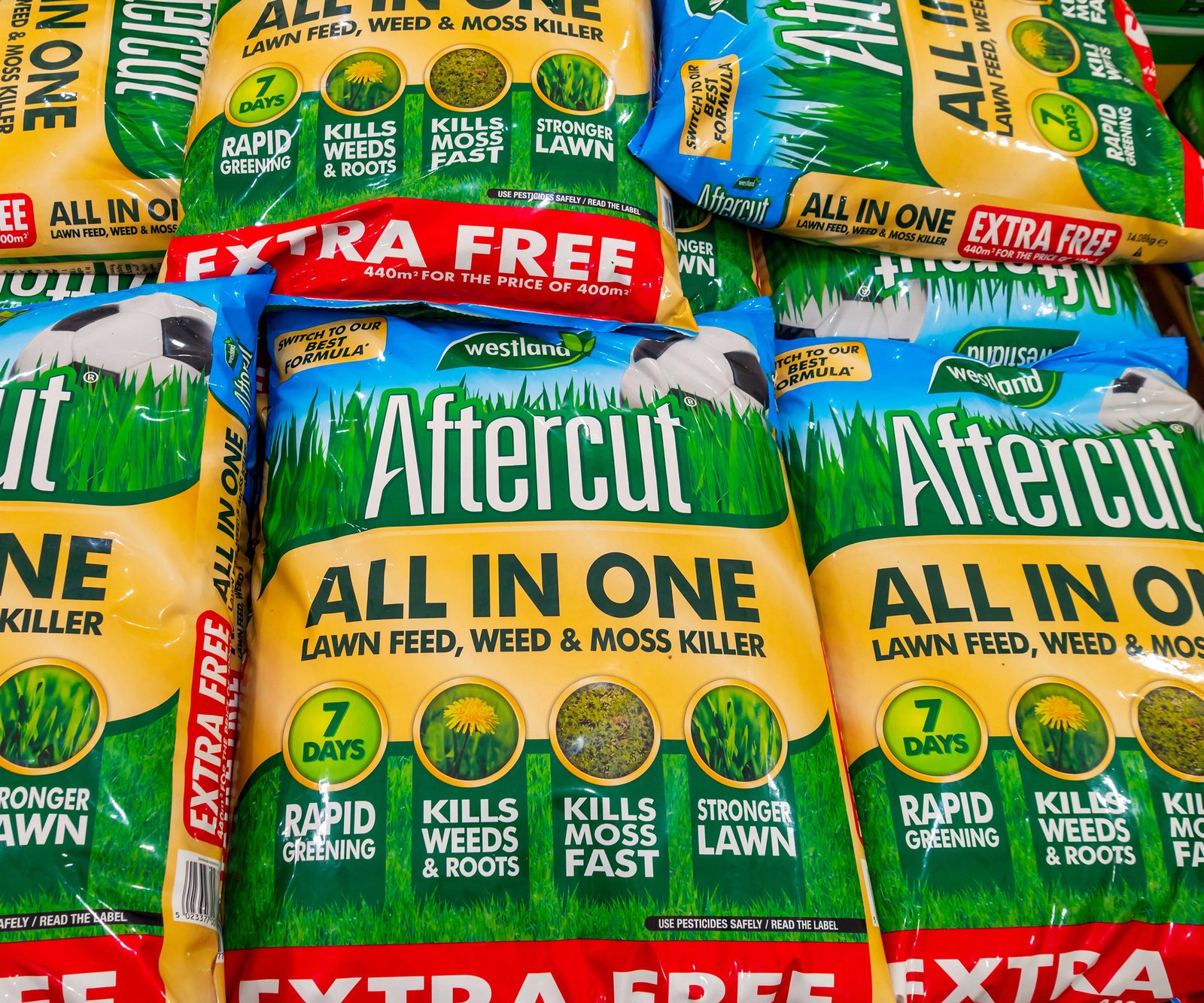 A stack of bags of Aftercut lawn feed weed and moss killer for sale in a garden centre