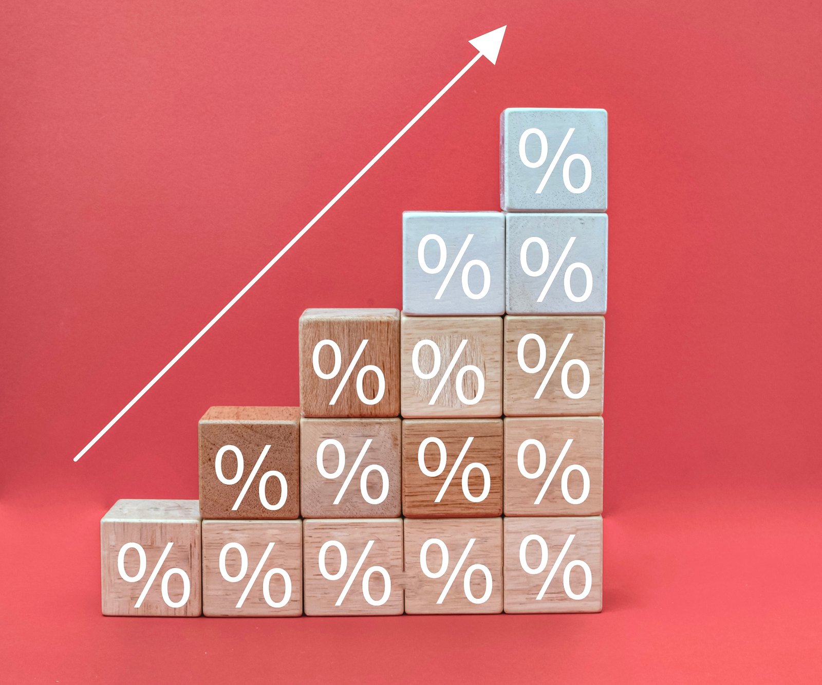 building blocks with percentage sign stacked up on red background with arrow drawn going in diagonal line upwards above blocks